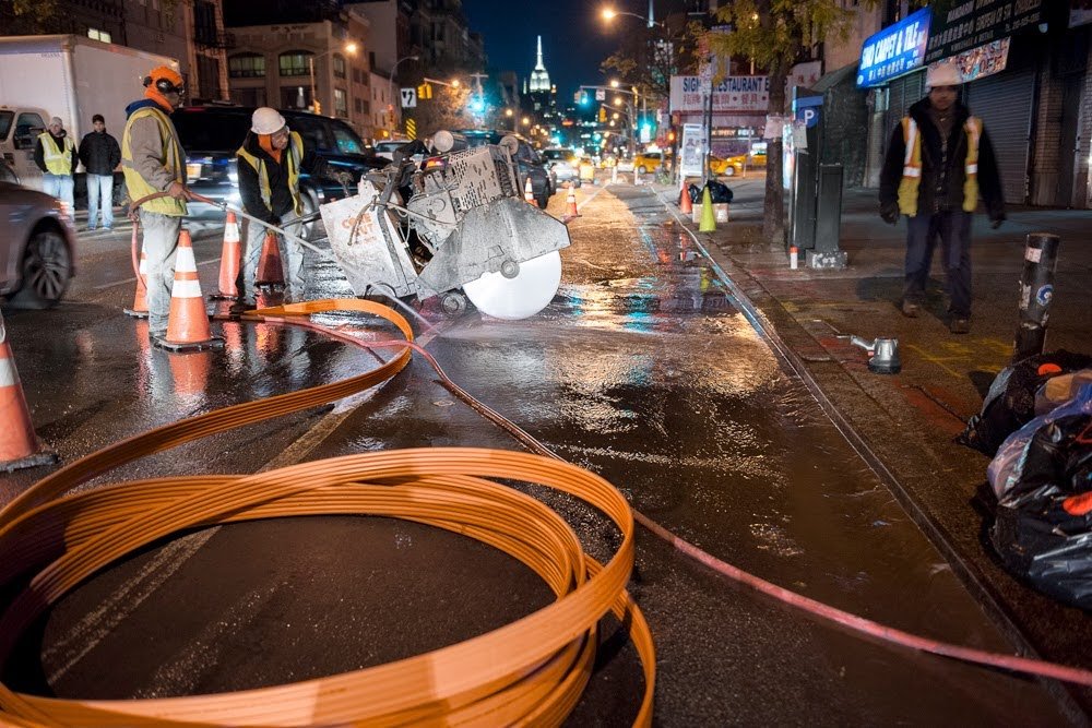 Stealth crew carrying out nighttime street construction beside coils of orange tubing.
