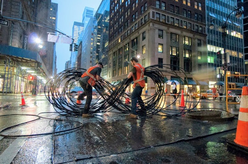Stealth crew handling coils of fiber cable on a New York roadway before underground installation.