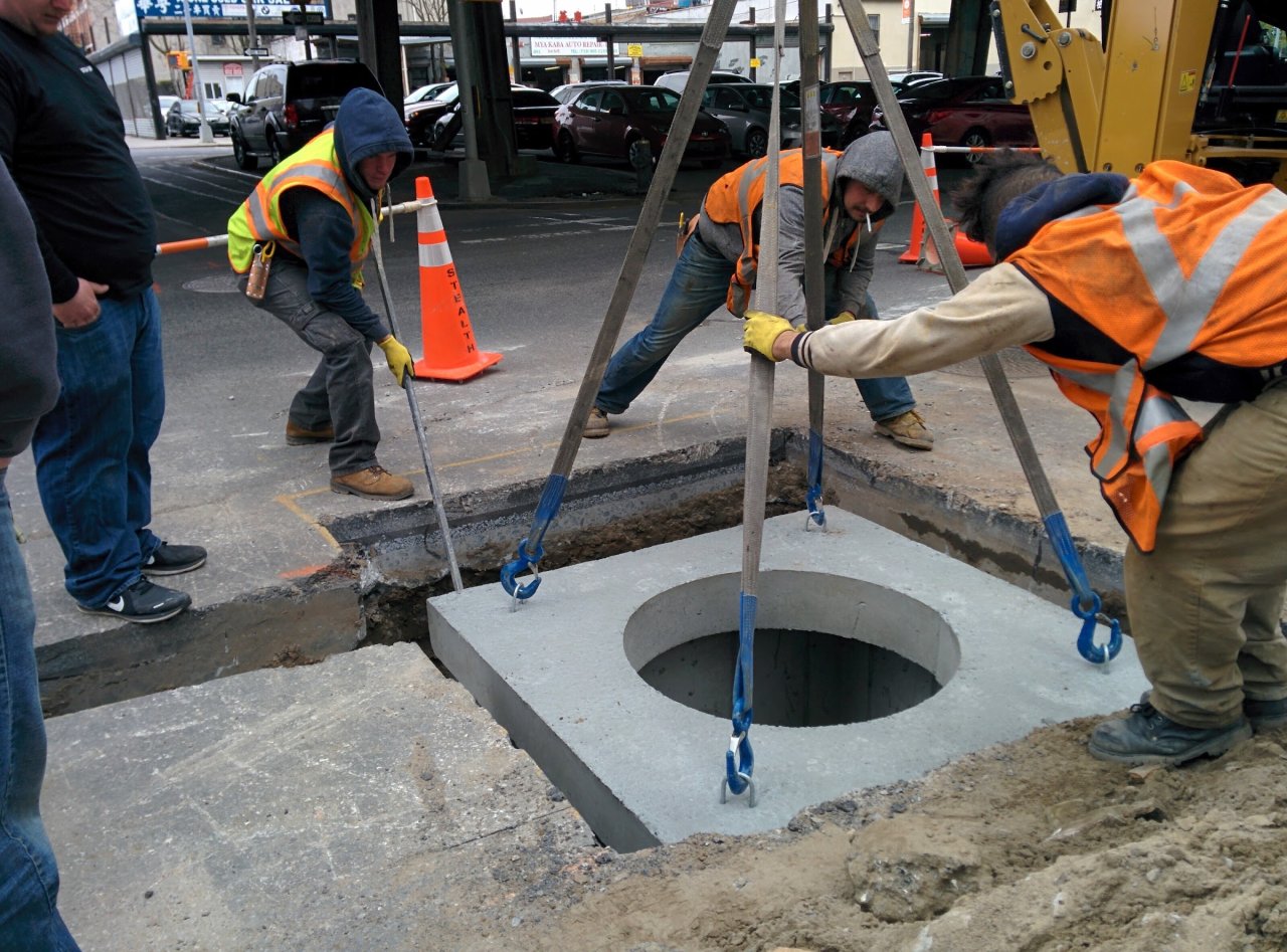 Stealth crew guiding a circular underground access structure into an excavated opening.