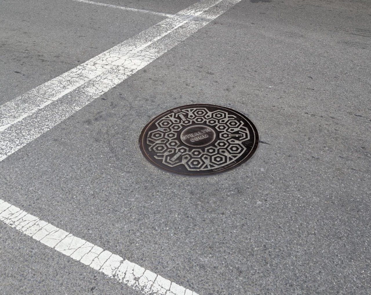 A patterned Stealth Communications manhole cover set into the roadway.