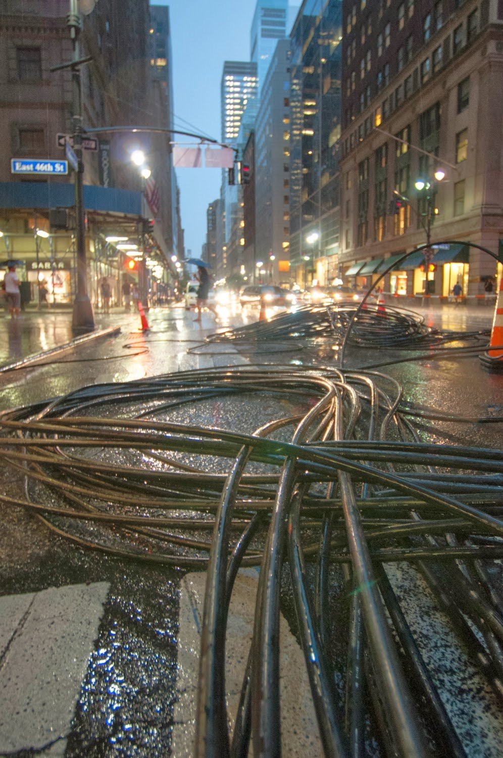 Coils of black cable across a rain-soaked Manhattan street at dusk.