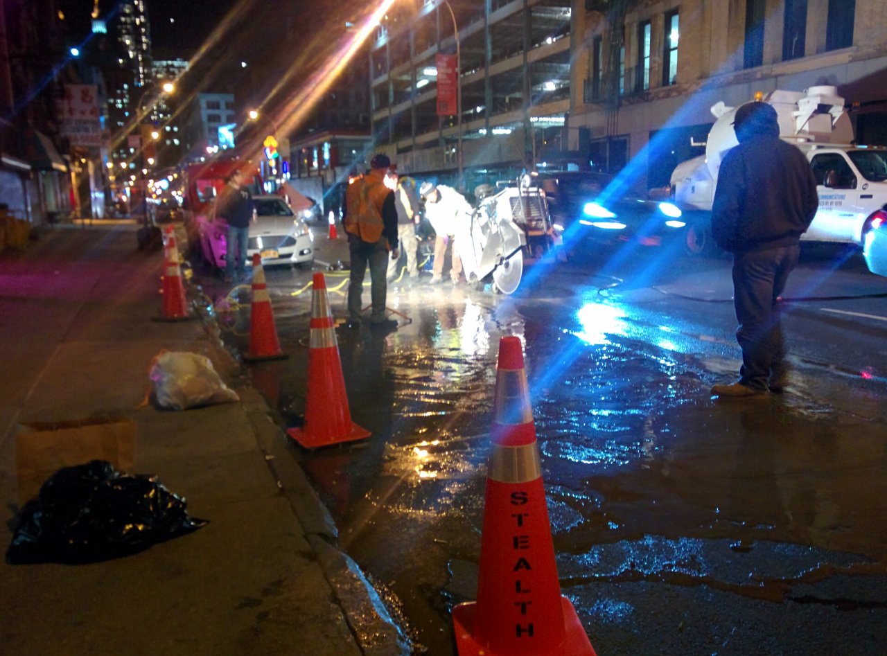 Stealth crew using a diamond blade street cutter on a city roadway at night, with Stealth traffic cones in the foreground.